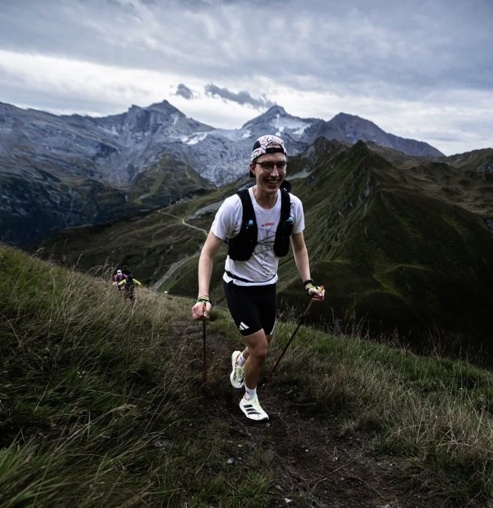 Marius lächelnd auf einem Bergtrail unter dunklen Wolken